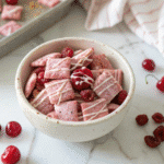 Cherry Cheesecake Puppy Chow in white bowl with pink coating and dried cherries