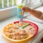 Toddler eating high-protein rose pasta sauce with shell pasta on colorful plate